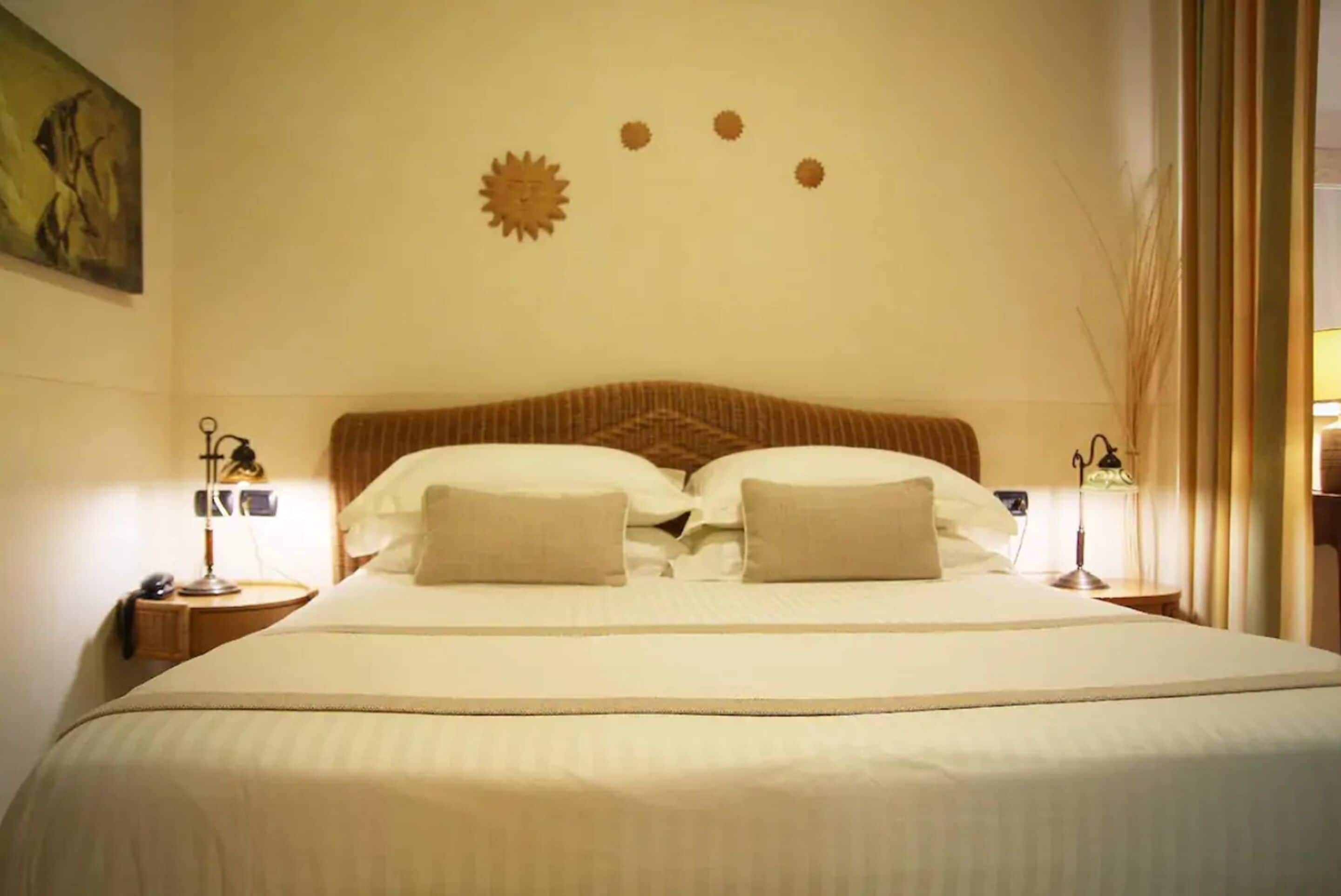 Una camera d'albergo con un letto grande, due comodini con lampade e una decorazione a parete sopra il letto.