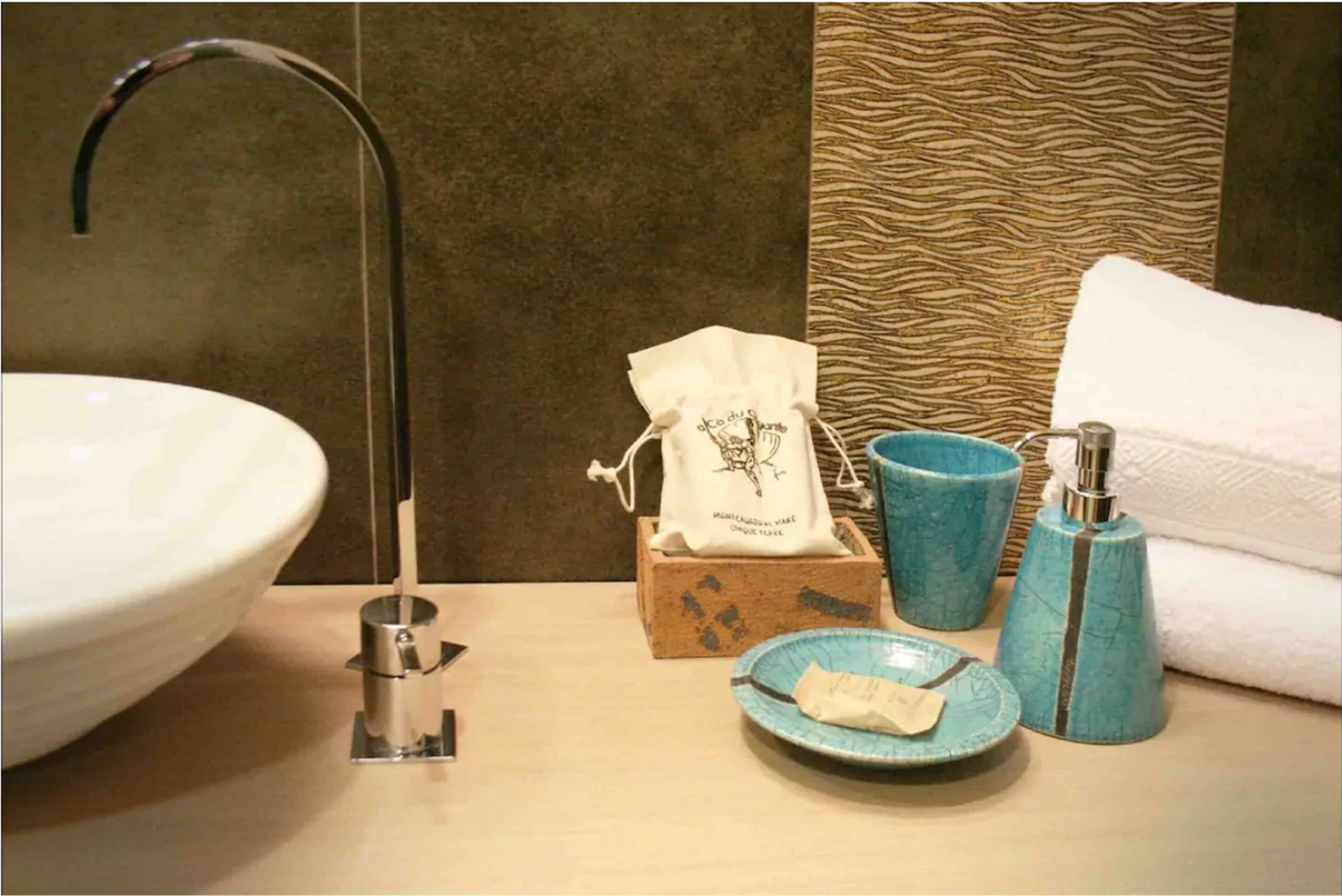 Un baño con lavamanos blanco, una toalla, un jabonera y un portacepillos.