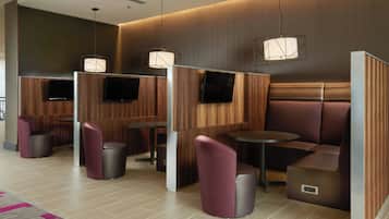 A modern hotel lobby with wooden panel partitions, seating areas, and a flat-screen TV mounted on the wall.