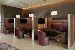 A modern hotel lobby with wooden panel partitions, seating areas, and a flat-screen TV mounted on the wall. - Courtyard by Marriott Rome Riverwalk (Rome)
