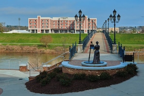 A Courtyard Marriott hotel with a statue in front, a river, and a pathway leading to the entrance. - Courtyard by Marriott Rome Riverwalk (Rome)