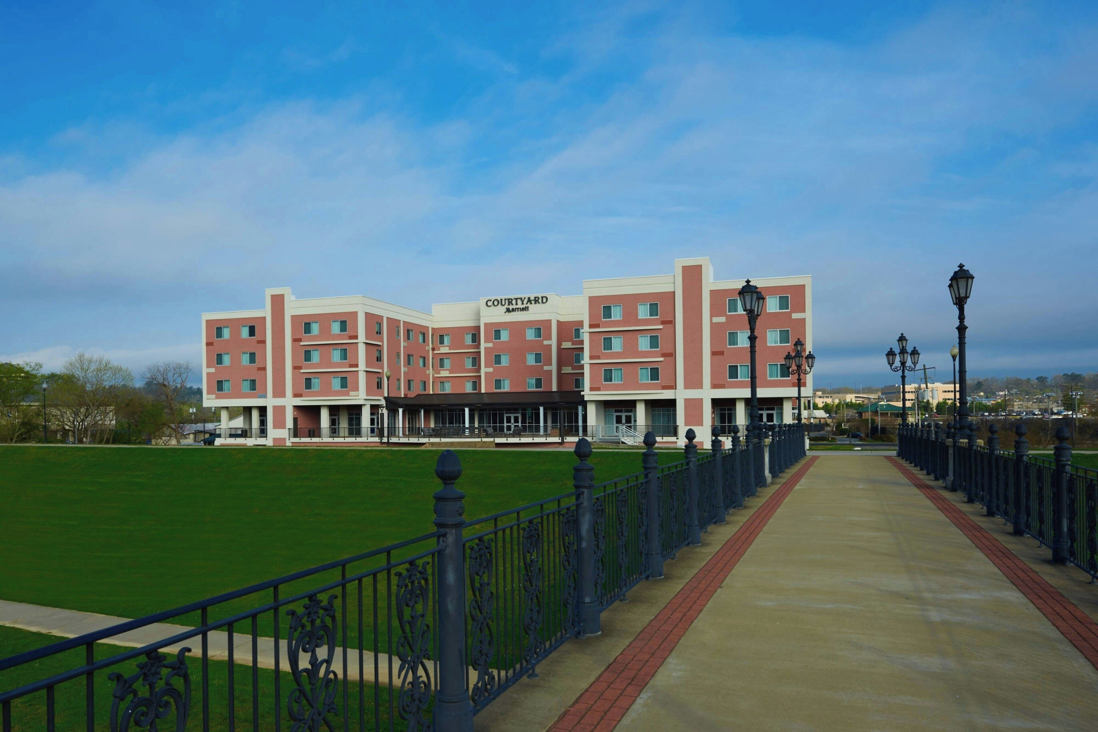 A Courtyard Marriott hotel with a green lawn in front, a brick pathway, and a metal fence.