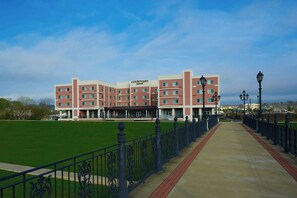 A Courtyard Marriott hotel with a green lawn in front, a brick pathway, and a metal fence. - Courtyard by Marriott Rome Riverwalk (Rome)