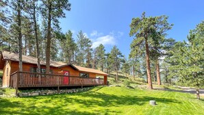A wooden cabin with a stone foundation, surrounded by a grassy area and tall pine trees. - Mountain Cabin Overlooking Breathtaking Riverfront and Valley Views  (Estes Park)