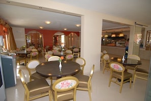 Un comedor con mesas y sillas redondas, una cocina al fondo y un espejo grande que refleja la habitación.