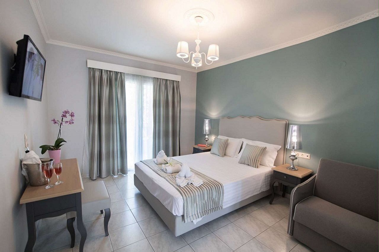 Ein Hotelzimmer mit einem großen Bett, einem Nachttisch mit Lampe, einer Couch, einem Fenster mit Vorhängen und einem an der Wand befestigten Fernseher.