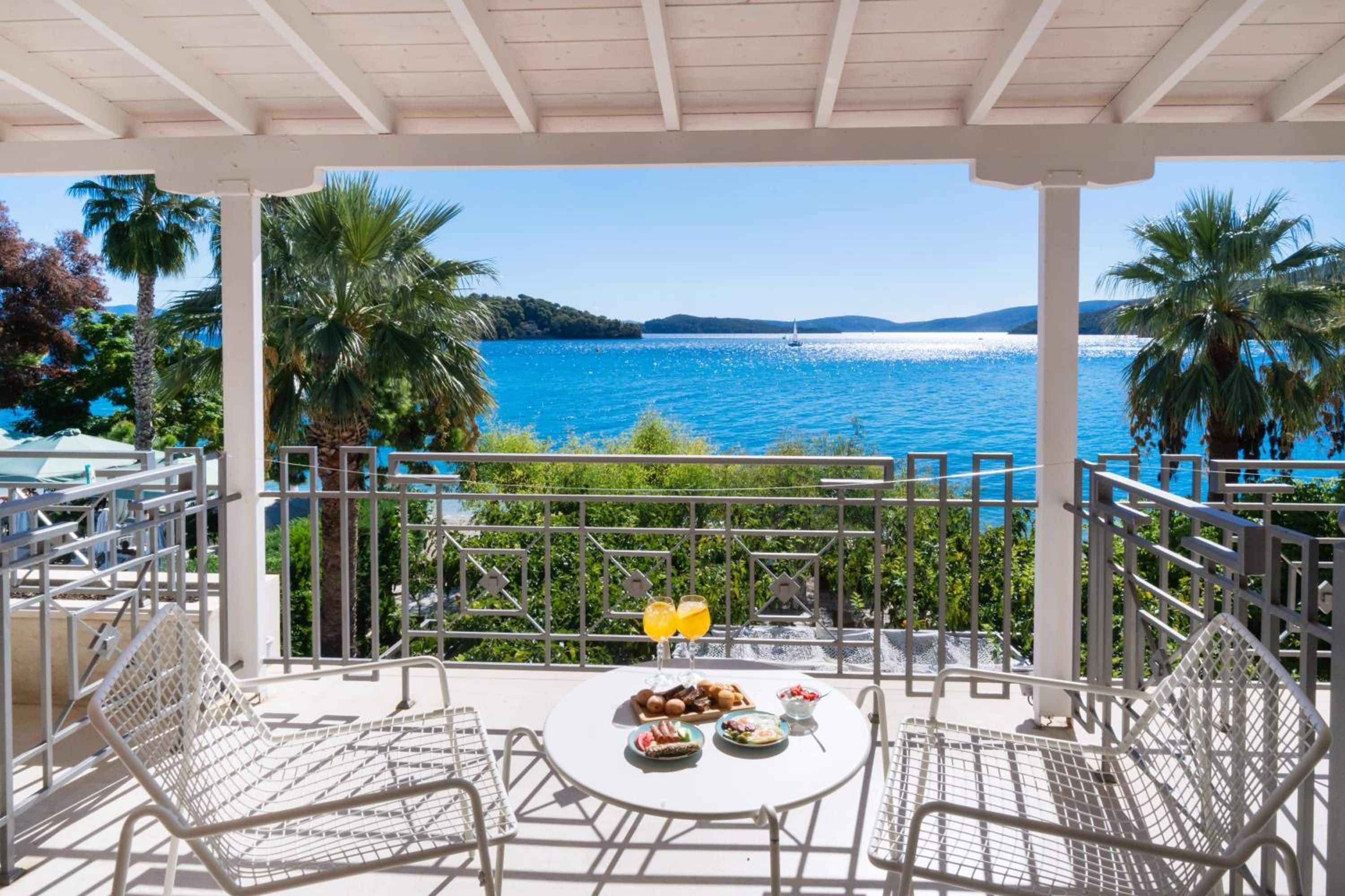Ein Balkon mit einem Tisch für zwei Personen, mit Blick auf ein Gewässer mit Booten und einer fernen Küste.