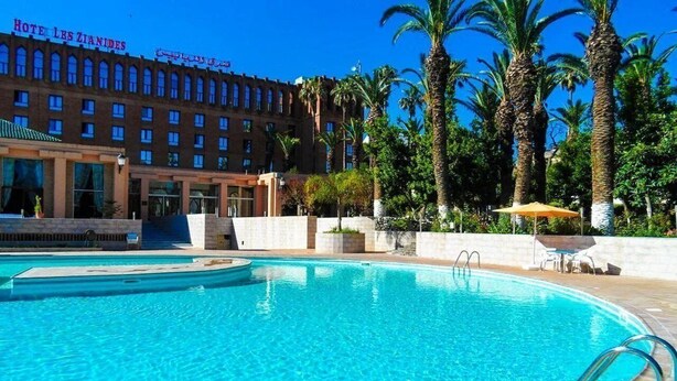 Un hotel con piscina, palmeras y un cielo azul despejado.