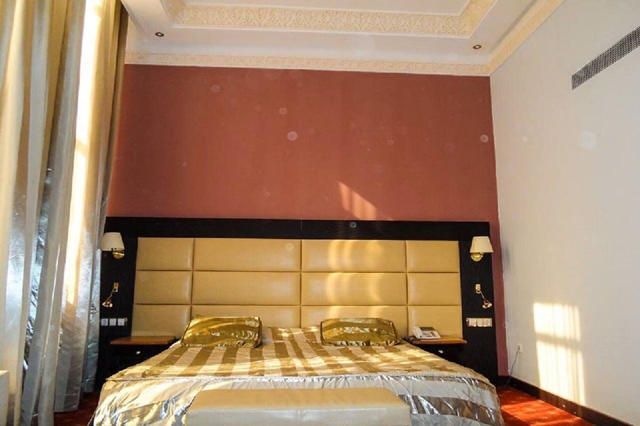Una habitación de hotel con una cama grande, cabecero, lámparas de noche y una ventana con cortinas.