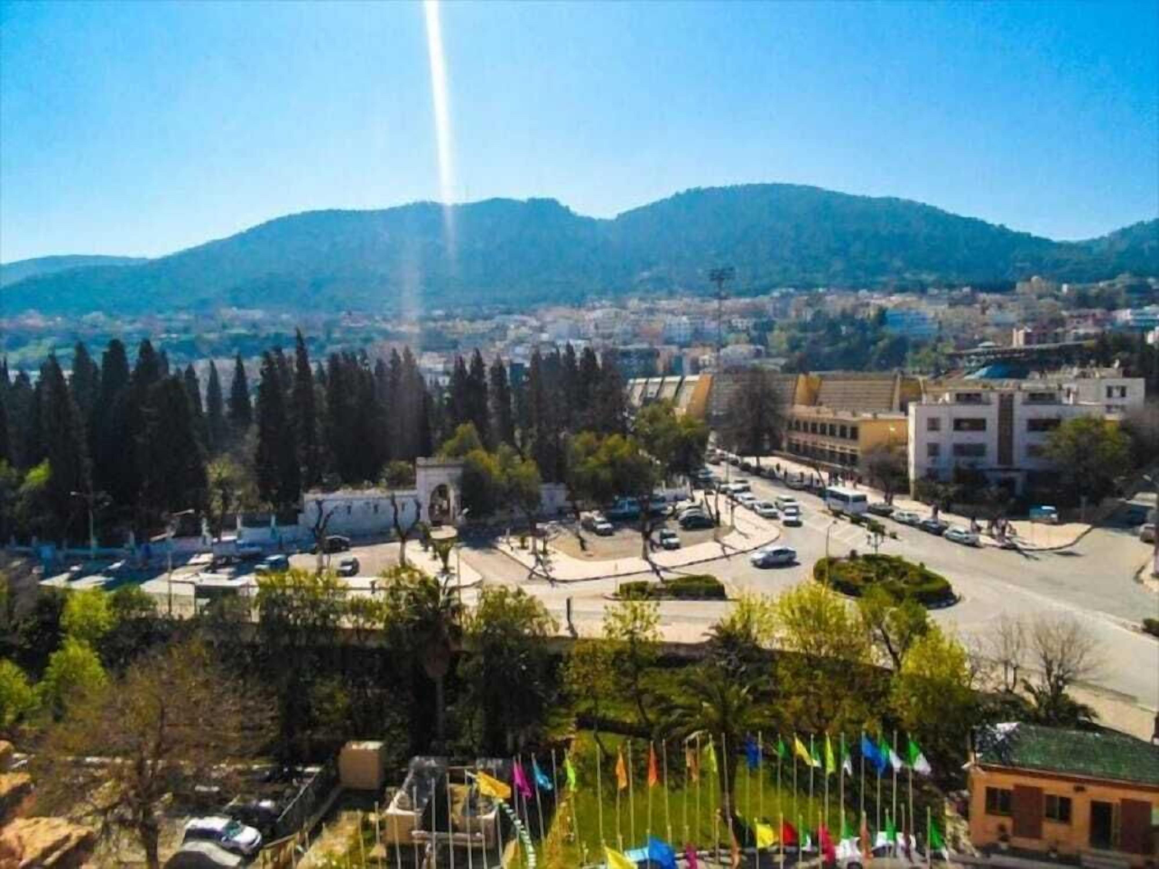 A cityscape with a prominent roundabout, buildings, and a mountain in the background.