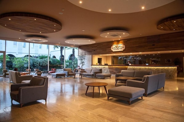 A spacious lobby with a reception desk, seating area, and large windows offering a view of the outdoors.