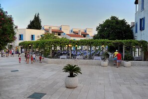 A public square with potted plants, a fountain, and people walking.