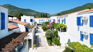 A narrow street with white buildings and blue shutters, surrounded by greenery and hills in the background. - Slovenska Plaza Resort 4 (Budva)