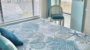 Une chambre avec un lit, une chaise et une vue sur la plage grâce à de grandes fenêtres.