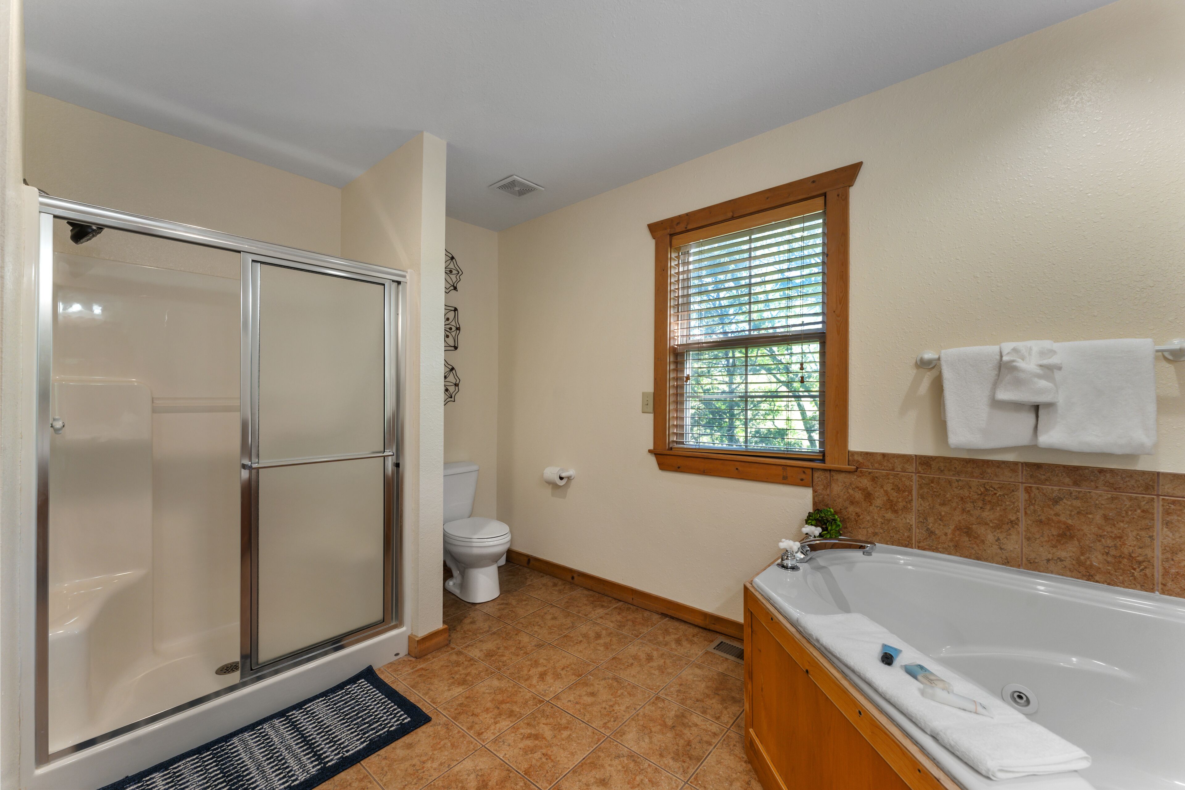 Ein Badezimmer mit Duschkabine, Toilette, Badewanne und einem Fenster mit Jalousien.