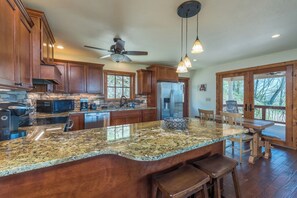 A kitchen with granite countertops, wooden cabinets, a central island, and a dining area with wooden furniture. - Among the Peaks | Spectacular Mtn Views+Fire Pit (Bakersville)