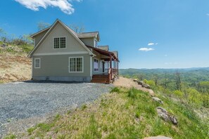 A two-story house with a porch, a gravel driveway, and a view of the surrounding landscape.