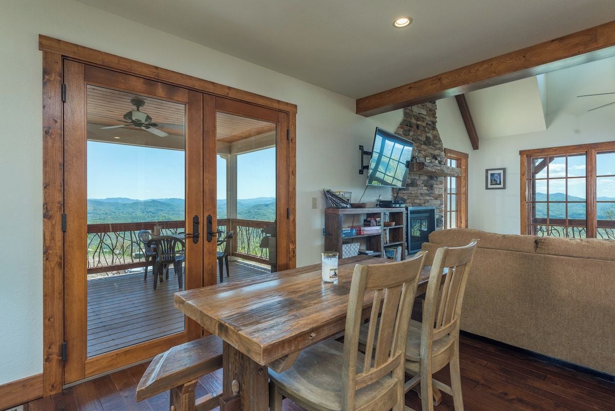 A wooden dining table with chairs, a sofa, and a stone fireplace.