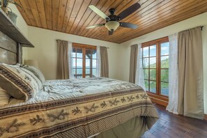 A bedroom with a bed, wooden ceiling, a ceiling fan, and large windows. - Among the Peaks | Spectacular Mtn Views+Fire Pit (Bakersville)