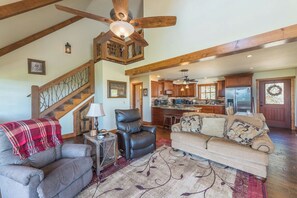 A spacious living area with a high ceiling fan, a staircase, a kitchen with modern appliances, and a cozy seating arrangement.