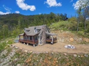A two-story house with a stone chimney, a porch, and a deck. - Among the Peaks | Spectacular Mtn Views+Fire Pit (Bakersville)
