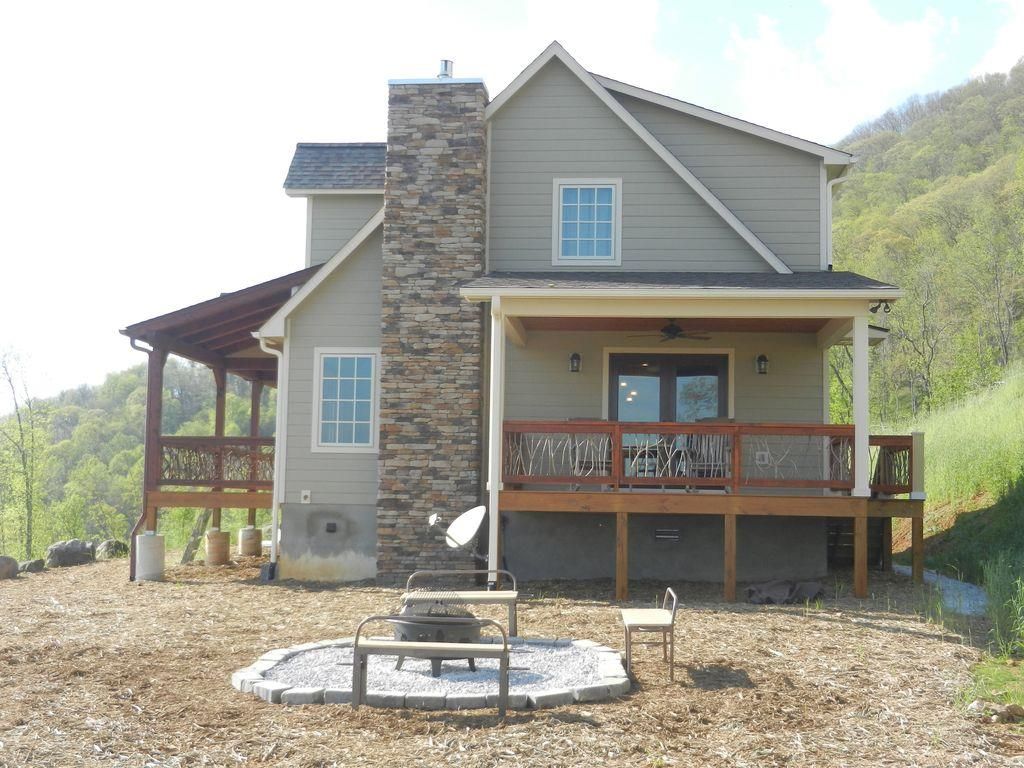 A two-story house with a stone chimney, a covered porch, and a fire pit in the yard.