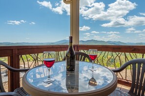 A round glass table with a bottle and two glasses of red wine, set against a scenic mountain backdrop. - Among the Peaks | Spectacular Mtn Views+Fire Pit (Bakersville)