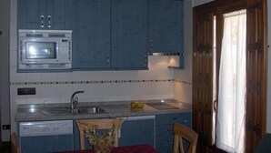 Una cocina con armarios azules, microondas, fregadero y una ventana con cortinas.
