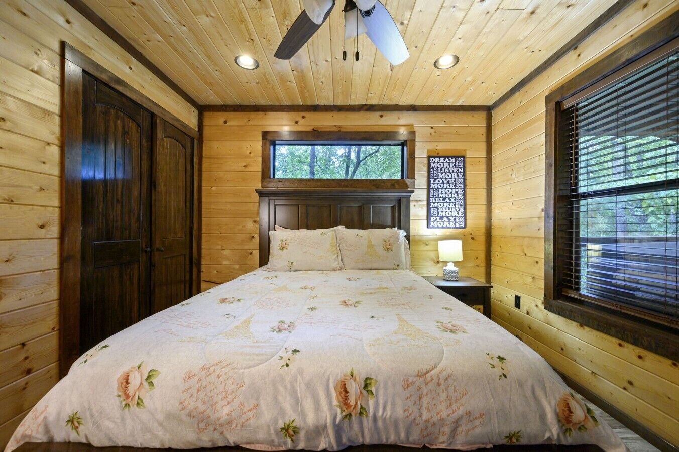 A wooden cabin bedroom with a bed, a window, and a ceiling fan.