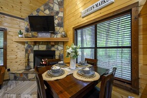 Un intérieur en bois agrémenté d’une cheminée en pierre, d’un téléviseur fixé au-dessus et d’une table à manger dressée avec de la vaisselle aux motifs noir et blanc.