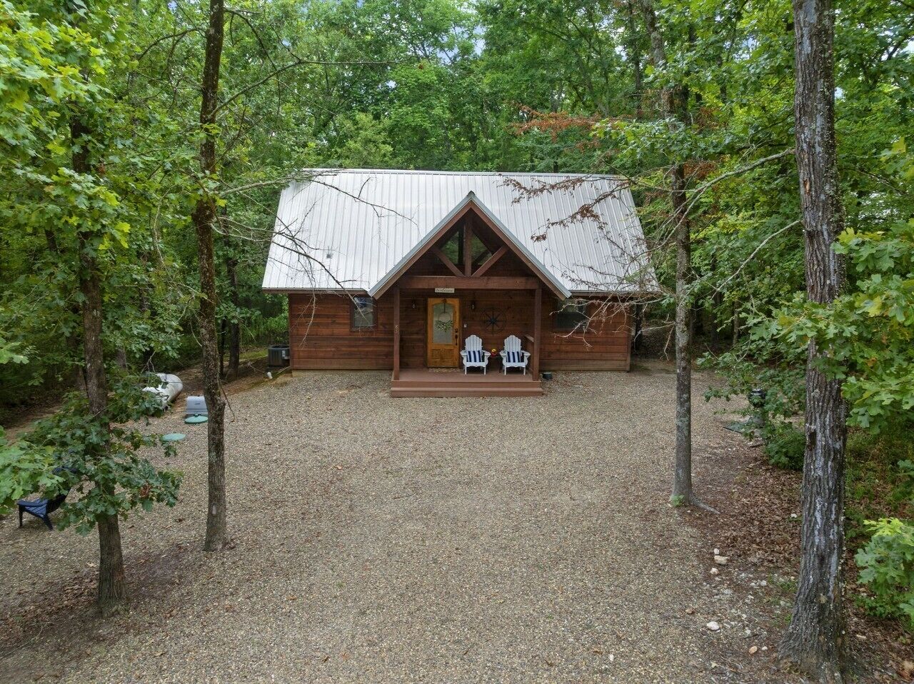 Une cabane en bois avec une allée en gravier, entourée d’arbres.