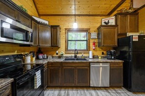 Una cocina con armarios de madera, electrodomésticos de acero inoxidable, encimera de granito y una ventana con persianas.