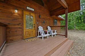 A wooden cabin with a porch, two Adirondack chairs, a welcome sign, and a decorative wreath on the door.