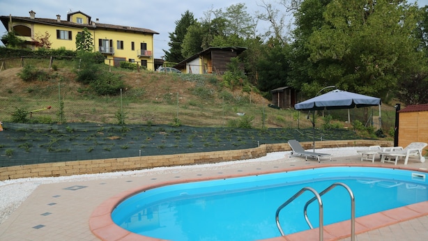 A swimming pool with a tiled deck, surrounded by a grassy area and a few trees. - Moscato apartment relax and culture (Nizza Monferrato)