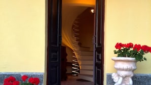 A hotel entrance with a number 113 sign, a spiral staircase, and two flower pots with red flowers. - Moscato apartment relax and culture (Nizza Monferrato)