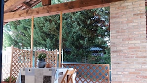 A covered outdoor patio with a table set for two, surrounded by wooden chairs. - Moscato apartment relax and culture (Nizza Monferrato)