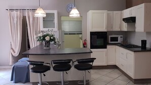A kitchen with a central island, three bar stools, a microwave, an oven, and white cabinets.