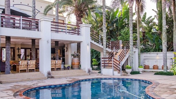 A two-story building with a pool, outdoor seating, and palm trees.