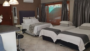 A hotel room with two beds, a small desk with a chair, a vase of flowers, and a window with curtains.