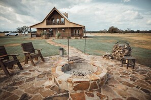 A rustic cabin with a stone fire pit, wooden chairs, and a large wooden deck. - 5-Star Private Cabin on 450+ acre gated/high fenced game ranch (Sulphur Bluff)