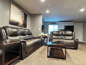 A living room with a brown leather sofa and armchair, a wooden coffee table, and a large painting on the wall.