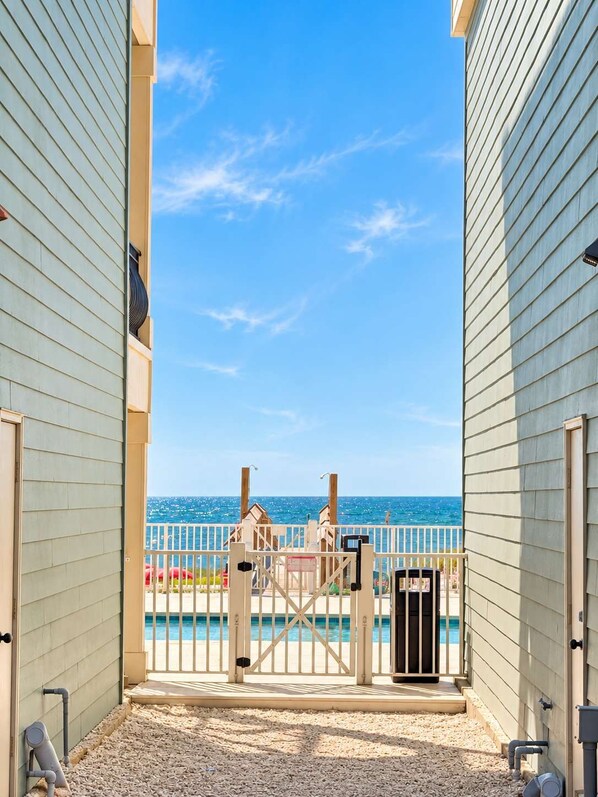 A view from a building's entrance to a pool area with a clear sky and ocean in the background.