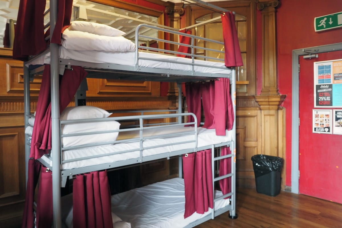 A bunk bed room with red curtains, a wooden floor, and a trash bin.