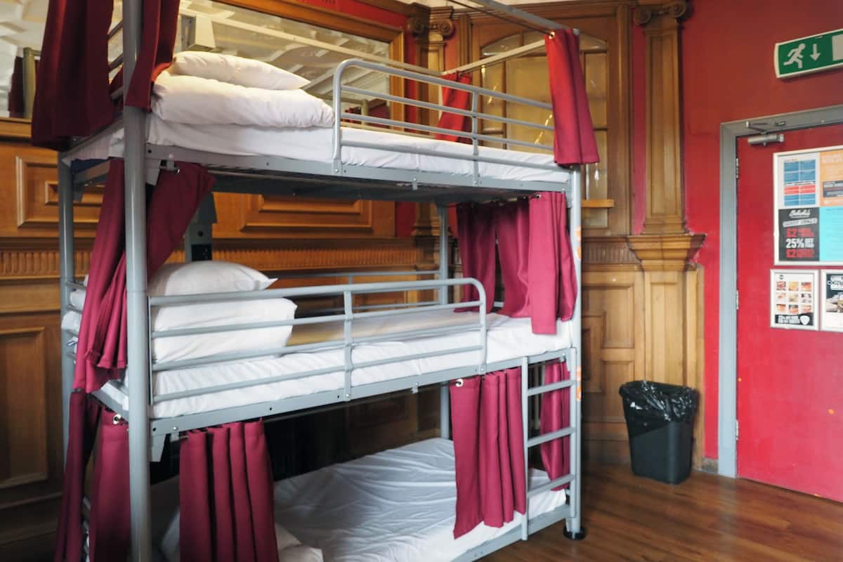 A bunk bed room with red curtains, a wooden floor, and a trash bin.