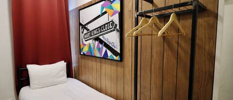 Un dormitorio con una cama, un panel de pared de madera, una obra de arte colorida y un perchero.
