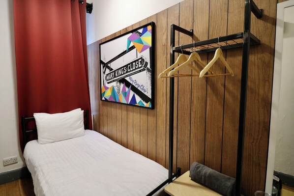 A bedroom with a bed, a wooden wall panel, a colorful artwork, and a clothing rack.