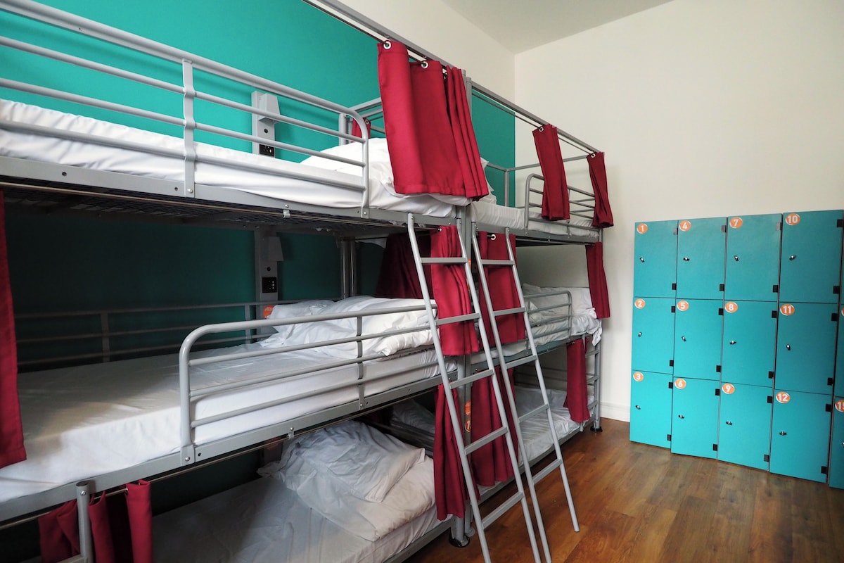 A bunk bed room with metal railings, red curtains, and a wooden floor.