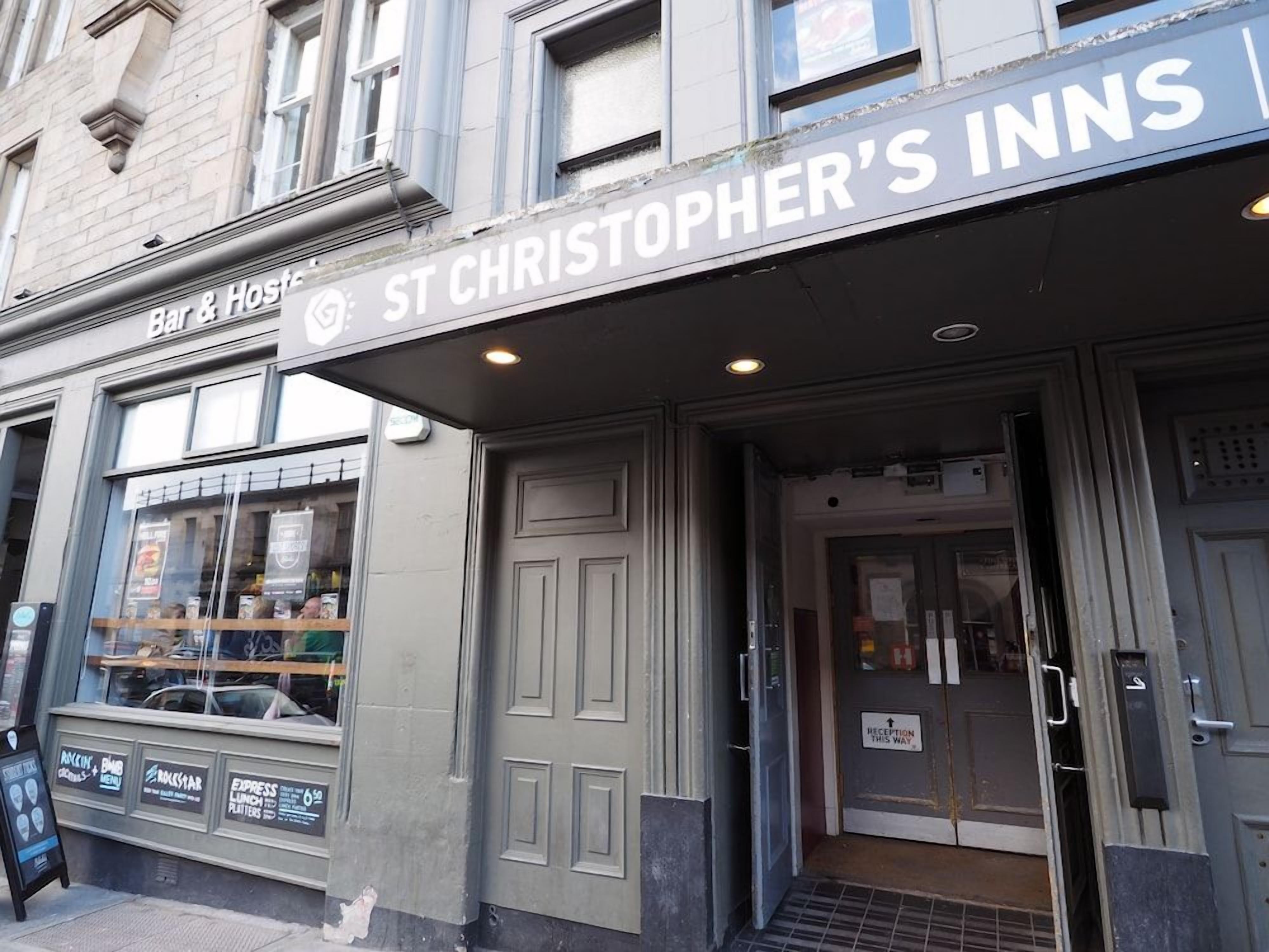 The exterior of St Christopher's Inns with a bar and hostelry sign, a reception desk, and a window displaying menu items.