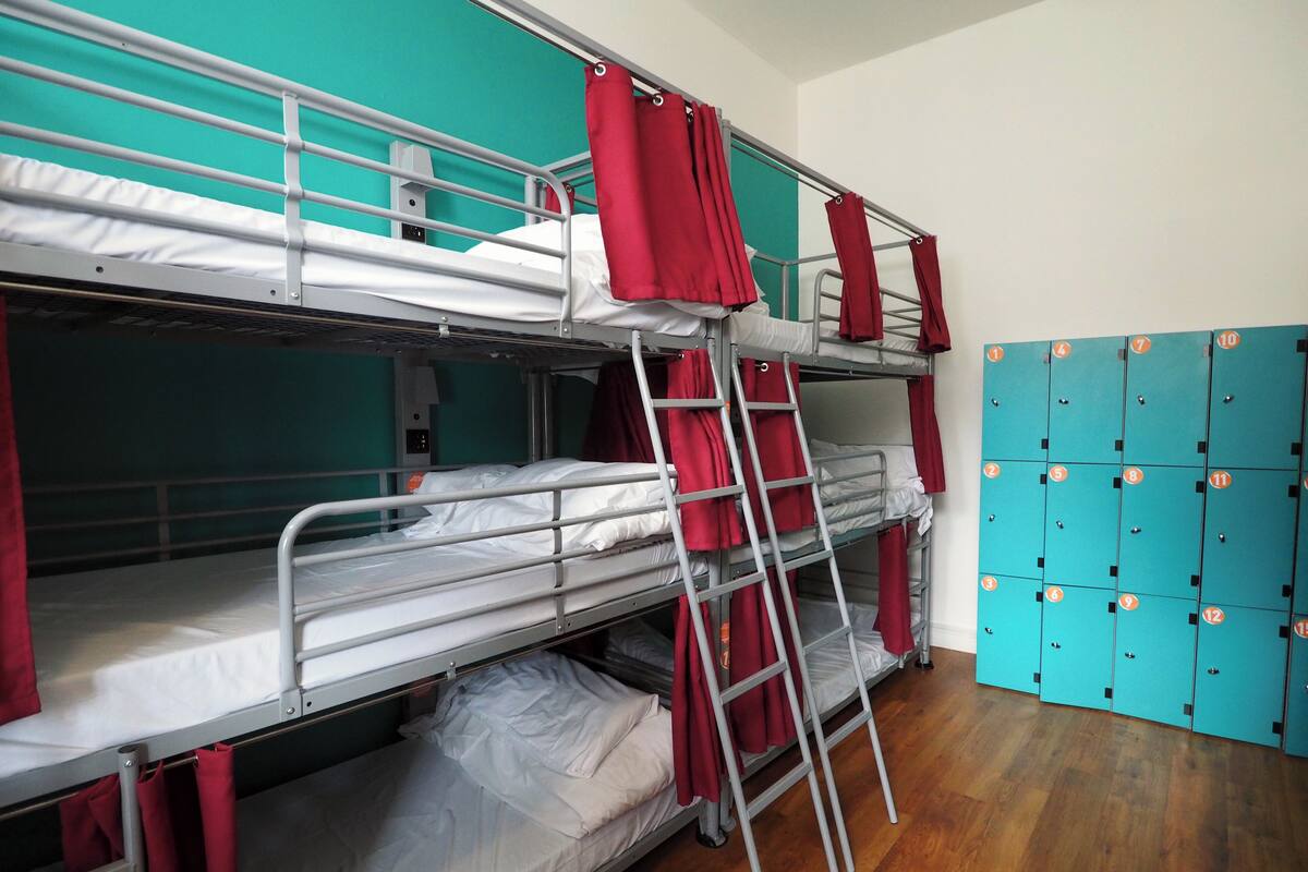 A bunk bed room with metal railings, red curtains, and a wooden floor.