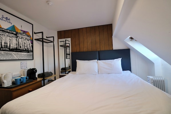 A hotel room with a large bed, a wooden headboard, a white wall with a framed picture, a small table with a kettle and cups, and a radiator. - St Christopher's Edinburgh Original (Edinburgh)